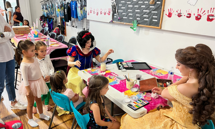 Two people dressed as Disney princesses painting with a group of kids