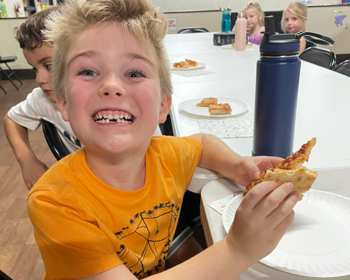 A boy eating pizza and smiling for the camera