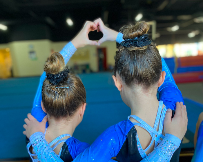 Two girls with arms around each other making a heart with their hands