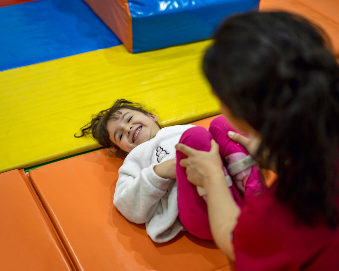 A toddler smiling as an instructor helps them with a stretch