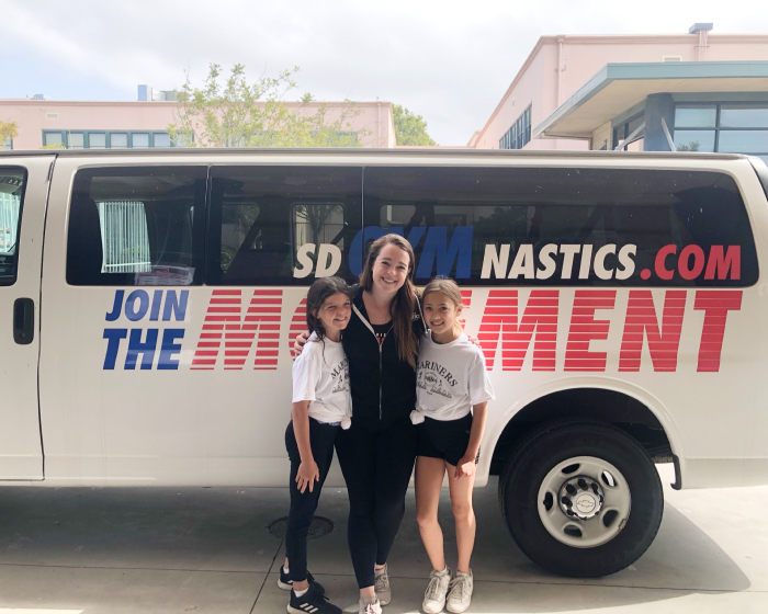 Two kids and a tutor in front of an S.D. Gym bus