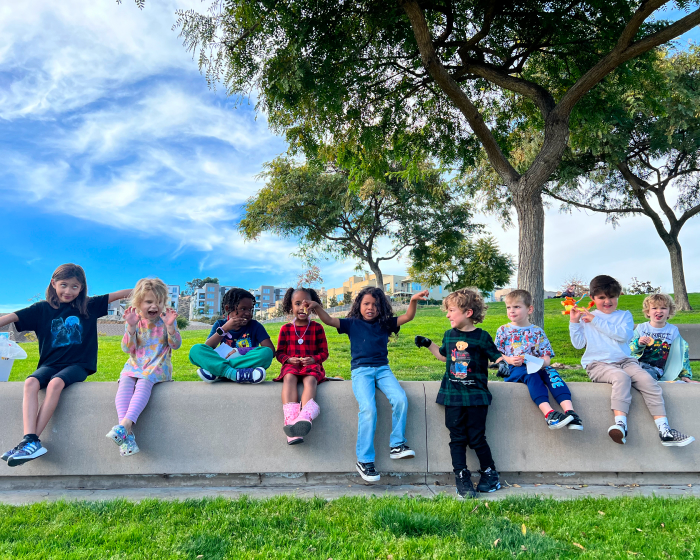 Preschool students sitting outside under a tree