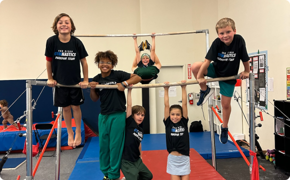 A group of kids hanging off a gymnastic bar, posing for a picture