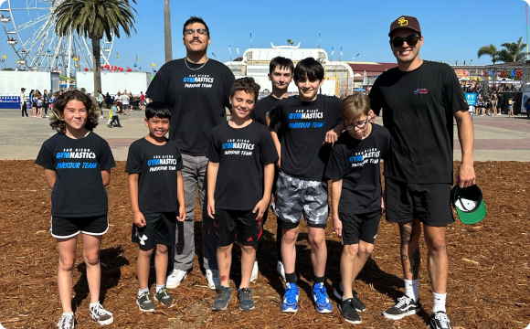 A group of kids and two instructors outside at the Del Mar fairgrounds posing for a pic