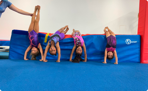 Four girls leaning over a gym mat upside down