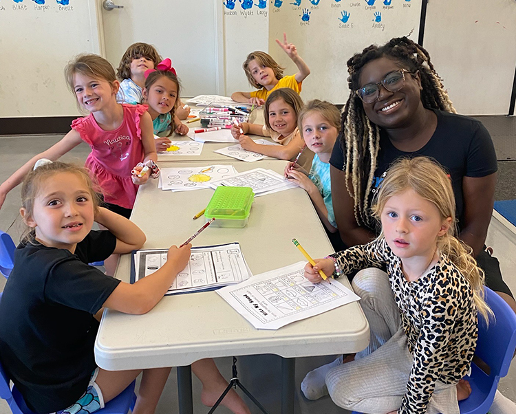 A preschool teacher sitting at a table with her students