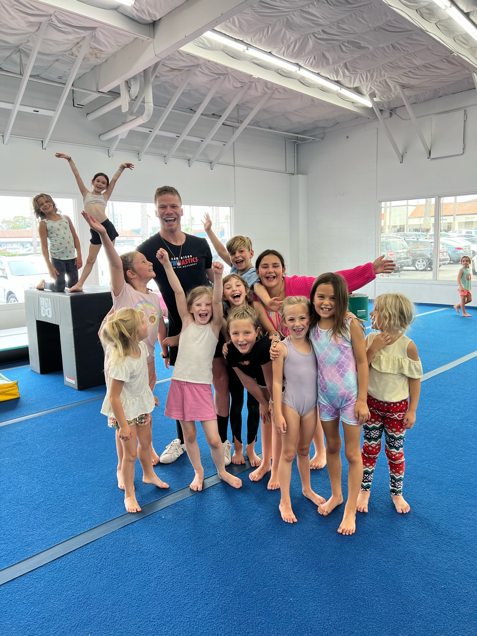 Gymnastics coach laughing with a bunch of young girls