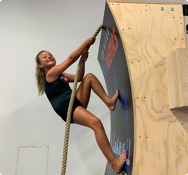 A girl climbing a rope up a wall.