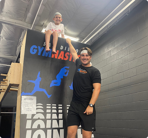 A staff member posing with a kid sitting on top of a ramp.